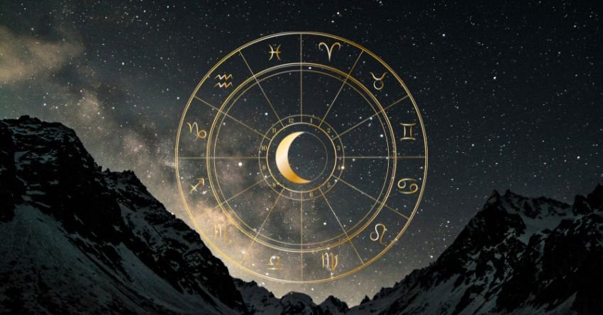 Golden zodiac wheel glowing above dark mountains beneath a cloudy, dramatic sky